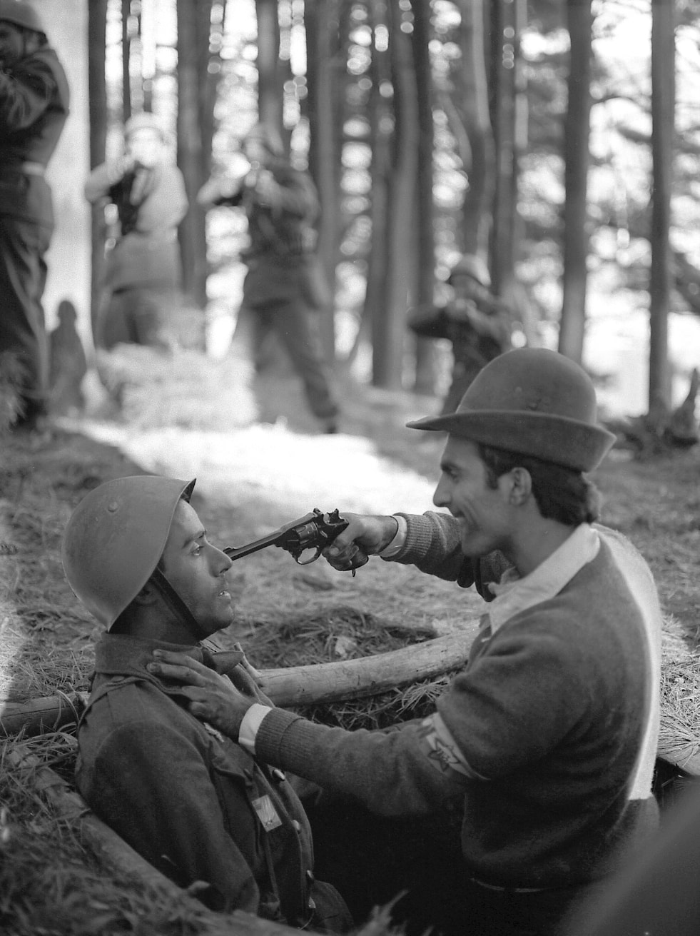 Italian partisan holds a pistol to the face of a soldier on the forest floor