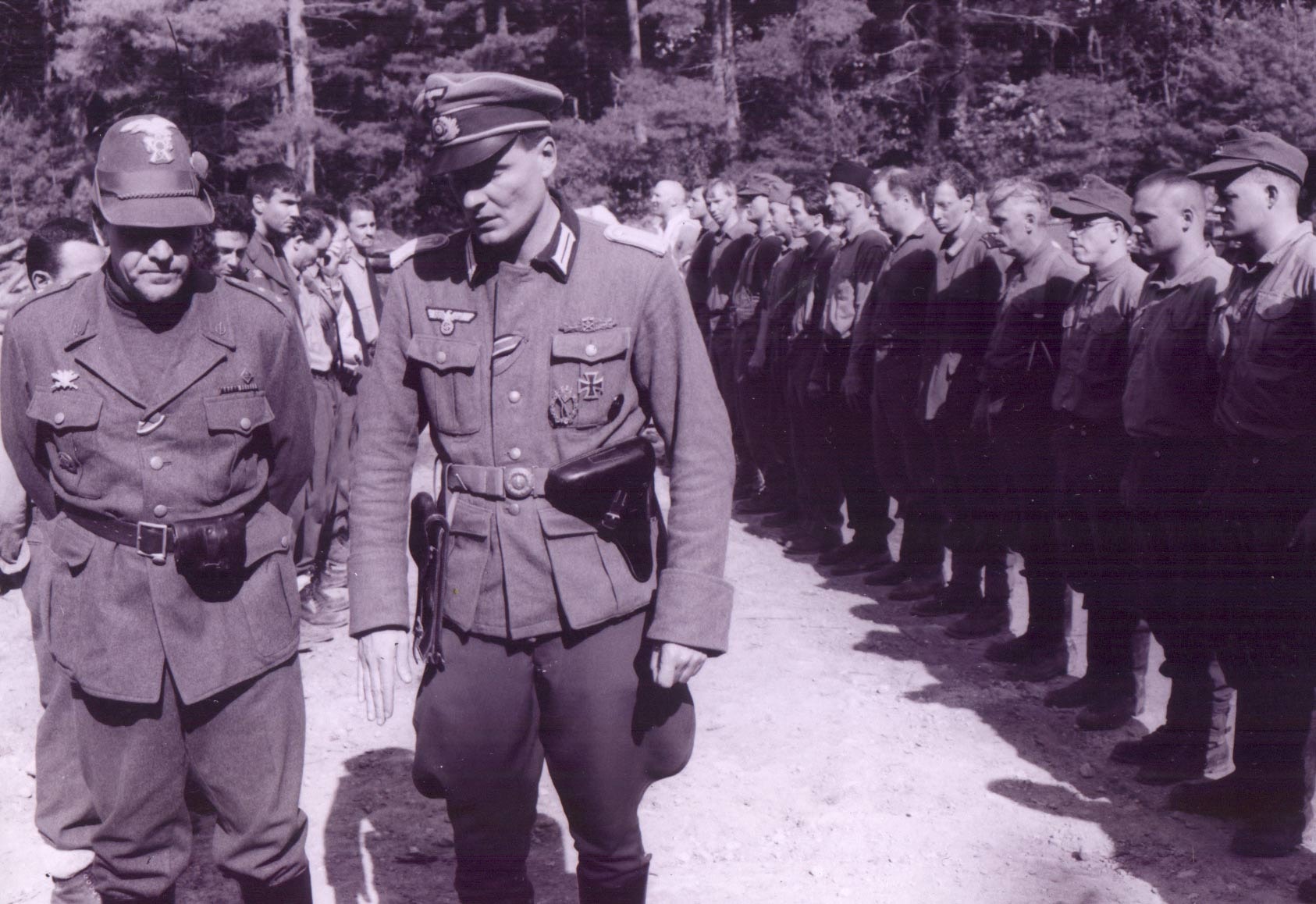 German and Italian officers walking past a line of soldiers in the forest