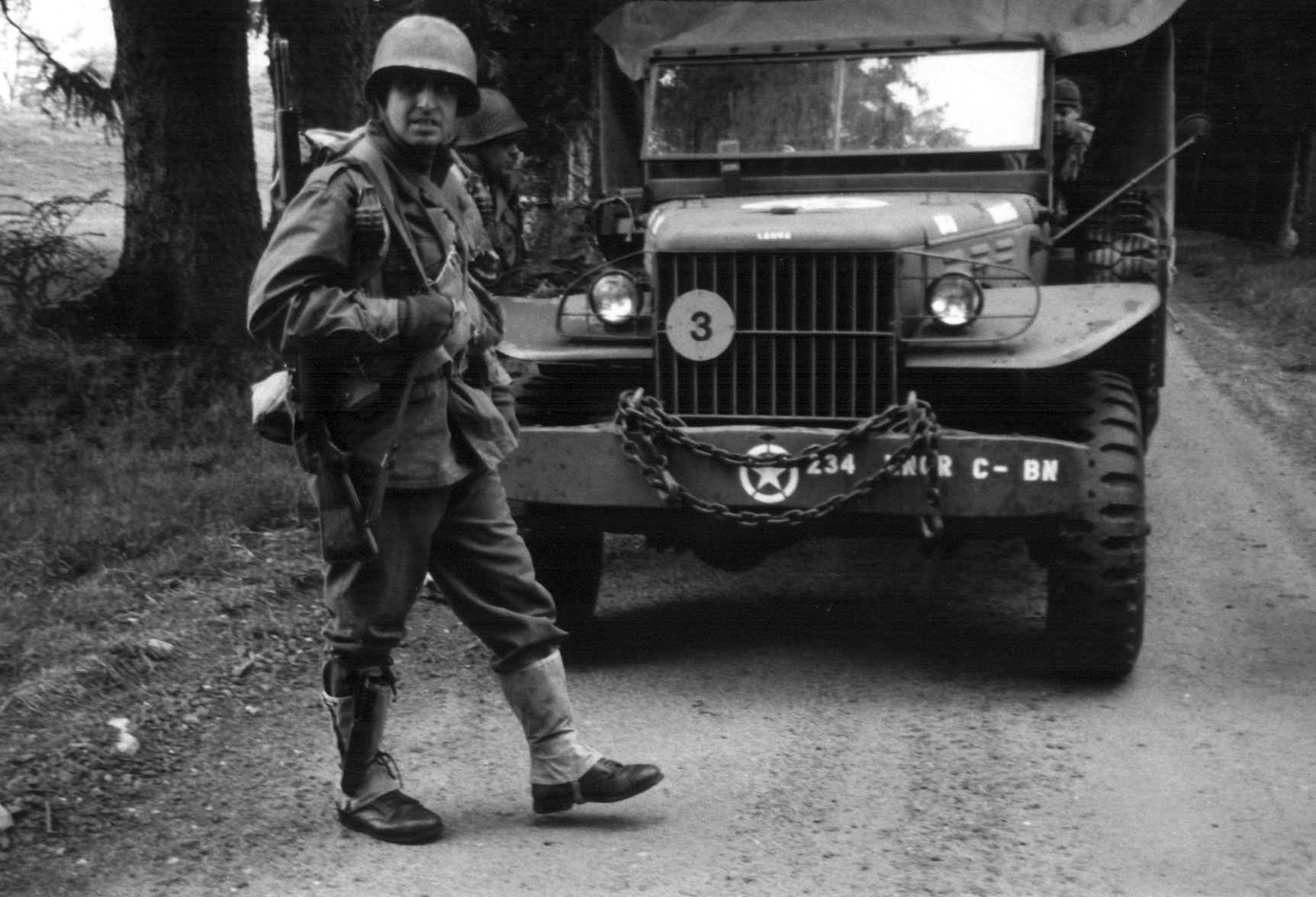 American soldier walking past a military vehicle on a country road
